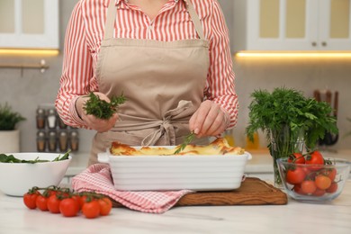 Photo of Woman putting rosemary onto lasagna at white marble table in kitchen, closeup