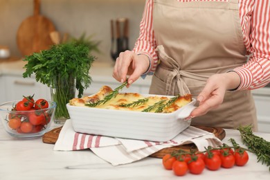 Photo of Woman putting rosemary onto lasagna at white marble table indoors, closeup