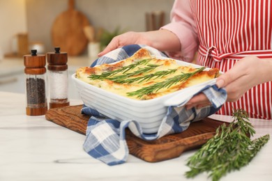 Photo of Woman putting baking dish with tasty lasagna onto white marble table indoors, closeup