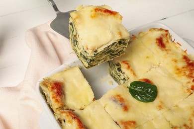 Photo of Taking piece of delicious spinach lasagne at white table, closeup