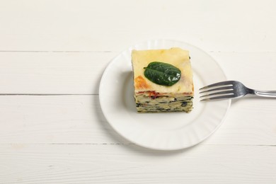 Piece of delicious spinach lasagne and fork on white wooden table