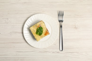 Photo of Piece of delicious spinach lasagne and fork on white wooden table, top view