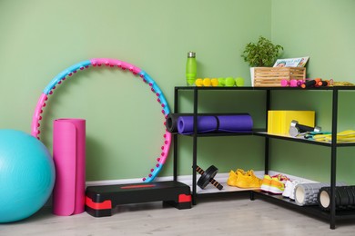 Different fitness equipment and sneakers near green wall indoors