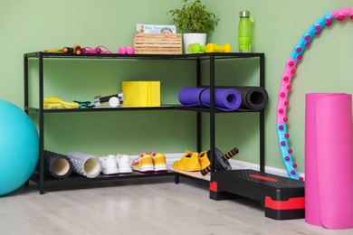 Different fitness equipment and sneakers near green wall indoors