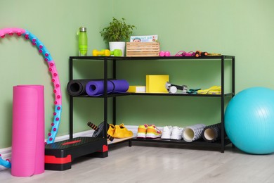 Different fitness equipment and sneakers near green wall indoors