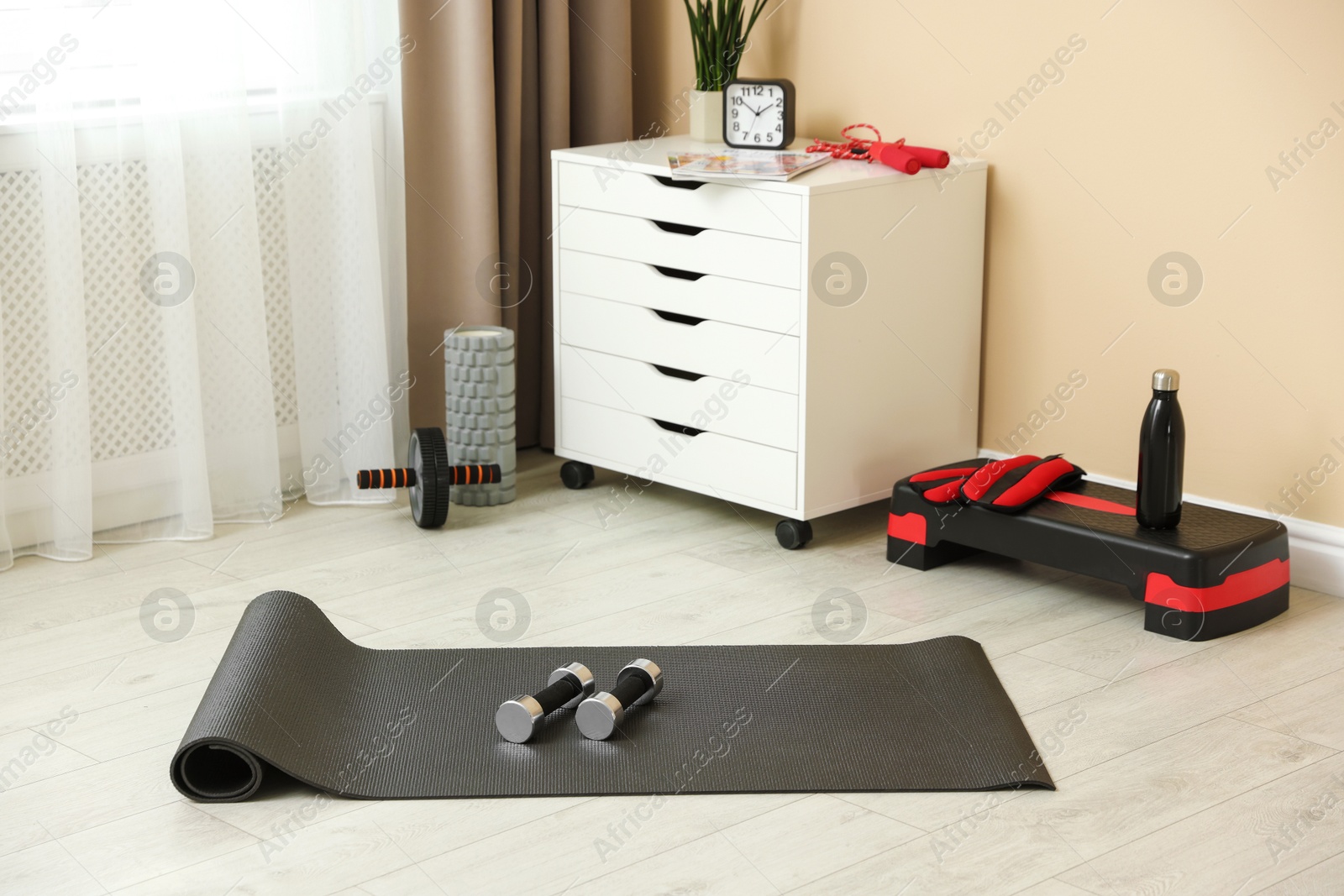 Photo of Different fitness equipment and chest of drawers indoors