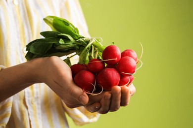 Photo of Woman with bunch of fresh radishes on green background, closeup