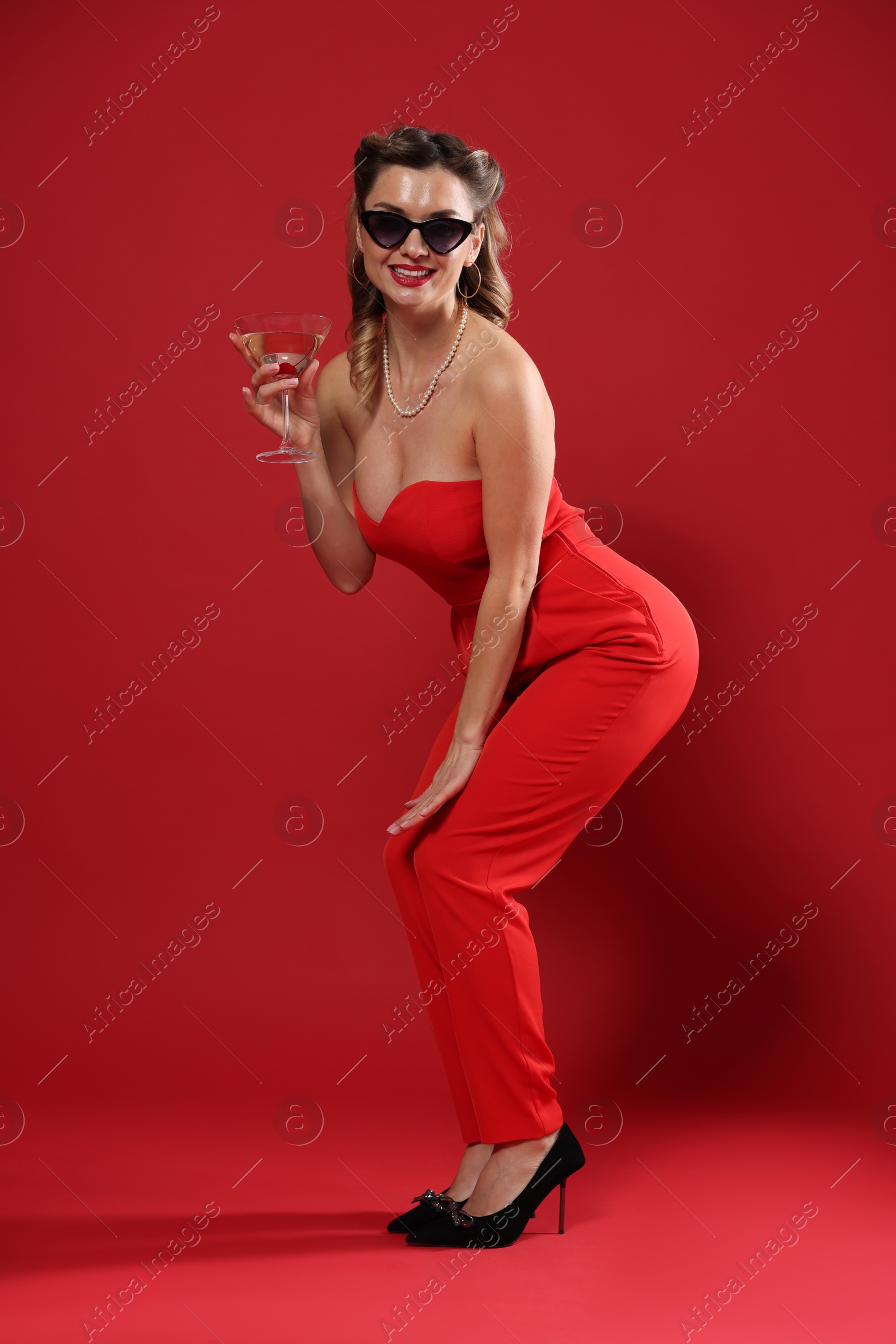 Photo of Happy woman with cocktail posing on red background. Pin-up vibes