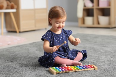 Photo of Cute little girl playing with toy xylophone on floor at home