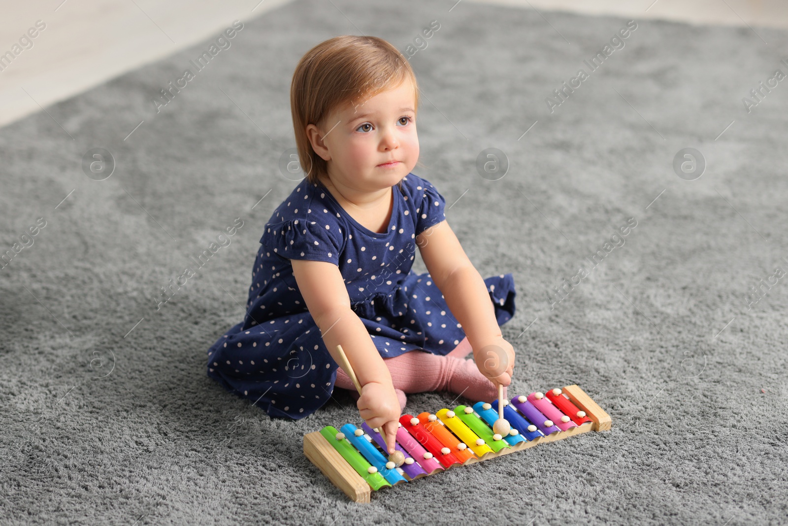 Photo of Cute little girl playing with toy xylophone on floor at home