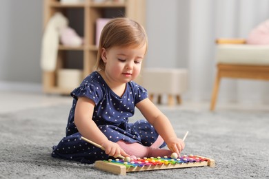 Cute little girl playing with toy xylophone on floor at home