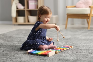 Cute little girl playing with toy xylophones on floor at home