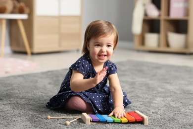 Photo of Cute little girl playing with toy xylophone on floor at home