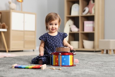 Photo of Cute little girl playing with toy musical instruments on floor at home