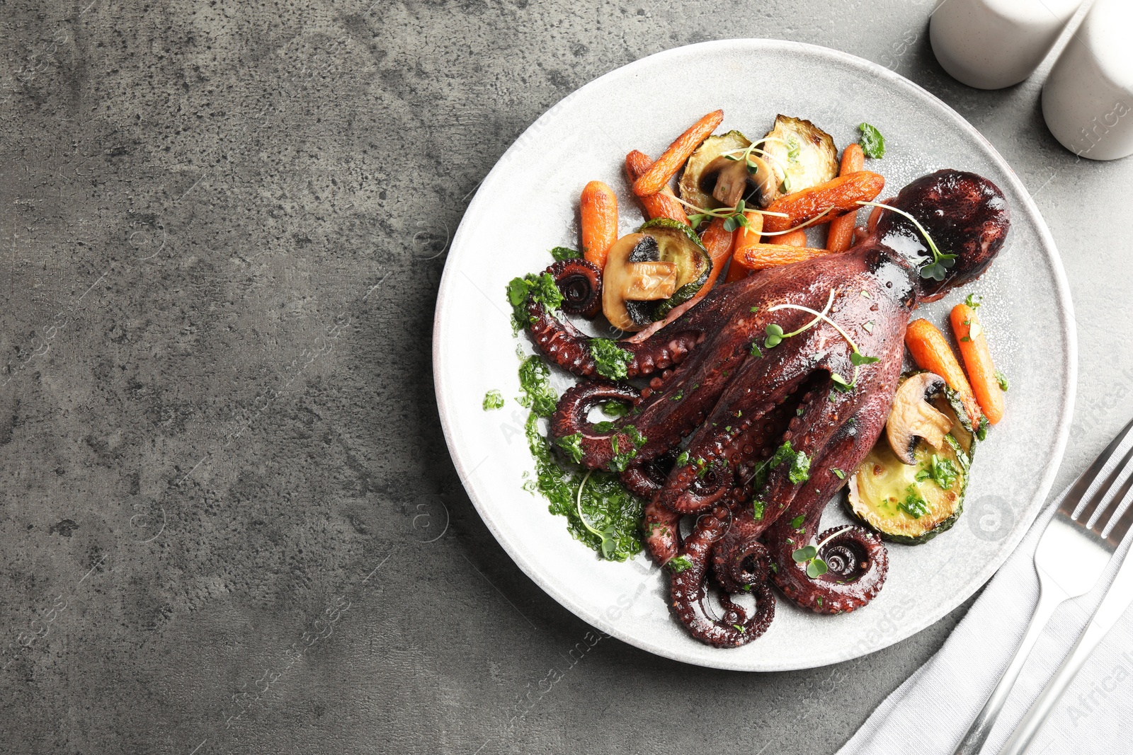 Roasted octopus served with vegetables and mushrooms on grey table, flat lay. Space for text Photo of Roasted octopus served with vegetables and mushrooms on grey table, flat lay. Space for text
