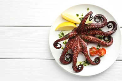 Fried octopus with herb sauce, lemon and tomatoes on white wooden table, top view. Space for text