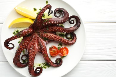 Photo of Fried octopus with herb sauce, lemon and tomatoes on white wooden table, top view