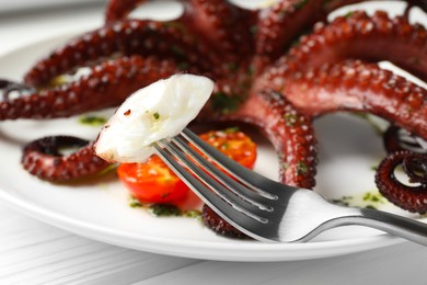 Eating tasty fried octopus with herb sauce at white wooden table, closeup