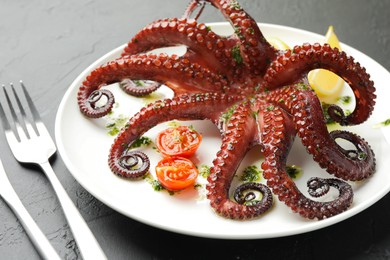 Fried octopus with herb sauce and tomatoes on dark textured table, closeup