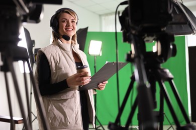 Happy young camerawoman with clipboard in modern film studio