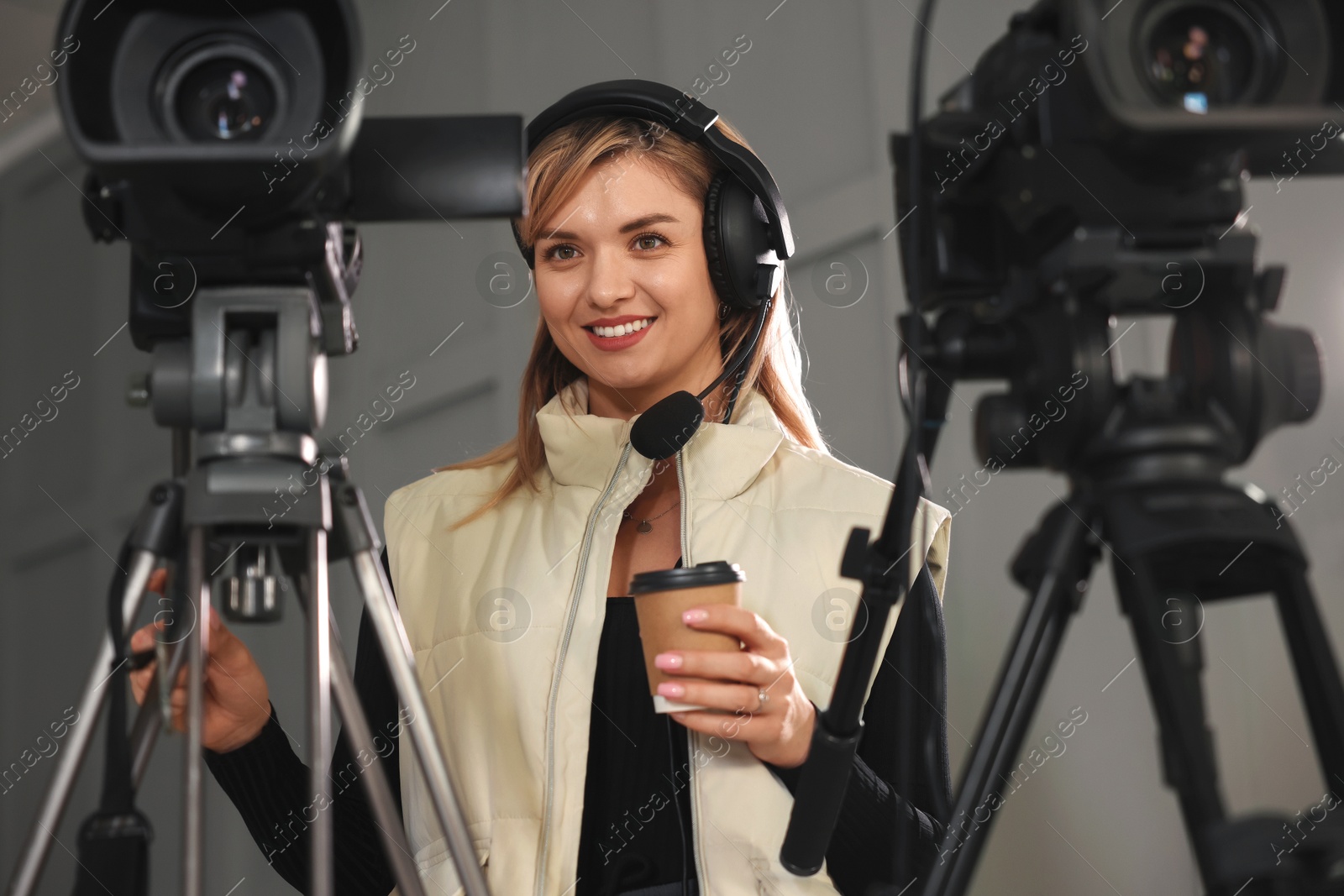 Photo of Happy young camerawoman with coffee working in modern film studio