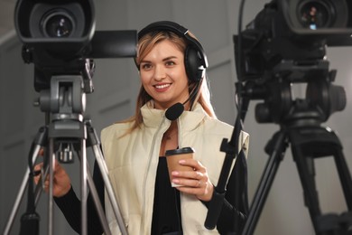 Happy young camerawoman with coffee working in modern film studio