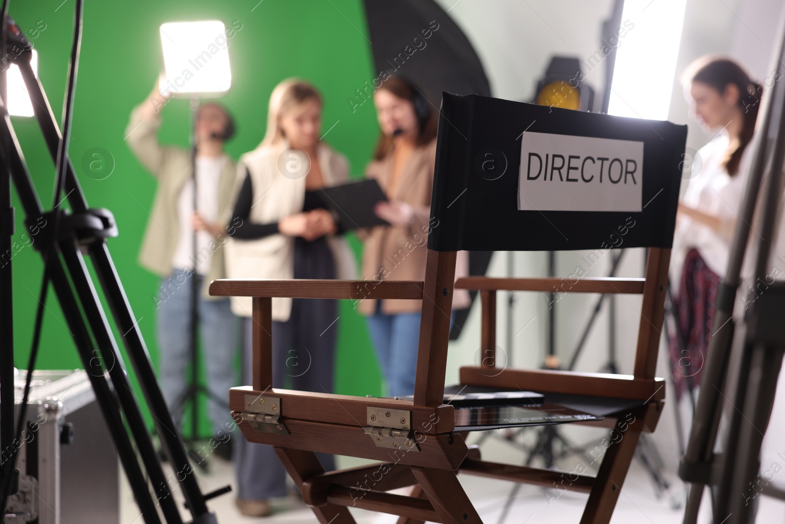 Photo of Group of people working in modern film studio, focus on chair with word Director