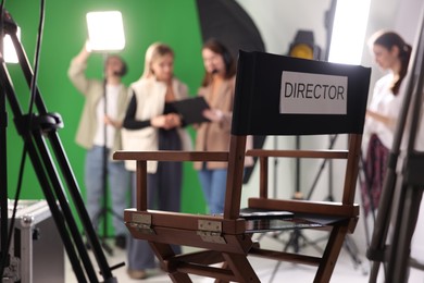 Photo of Group of people working in modern film studio, focus on chair with word Director