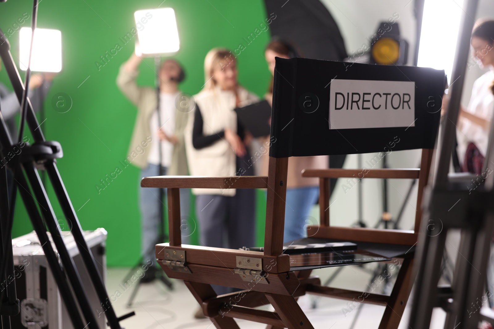 Photo of Group of people working in modern film studio, focus on chair with word Director