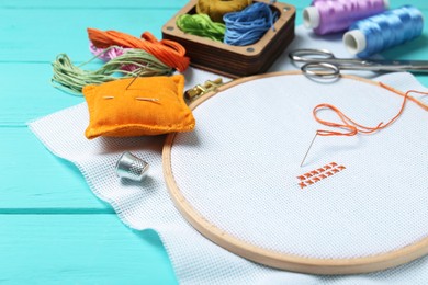 Photo of Embroidery. Canvas with cross stitches and supplies on turquoise wooden table, closeup