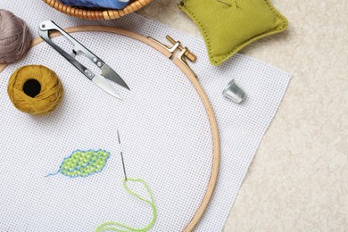 Photo of Embroidery and different sewing accessories on beige textured table, flat lay