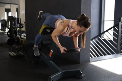 Athletic woman training with weight plate on t-bar row machine in gym