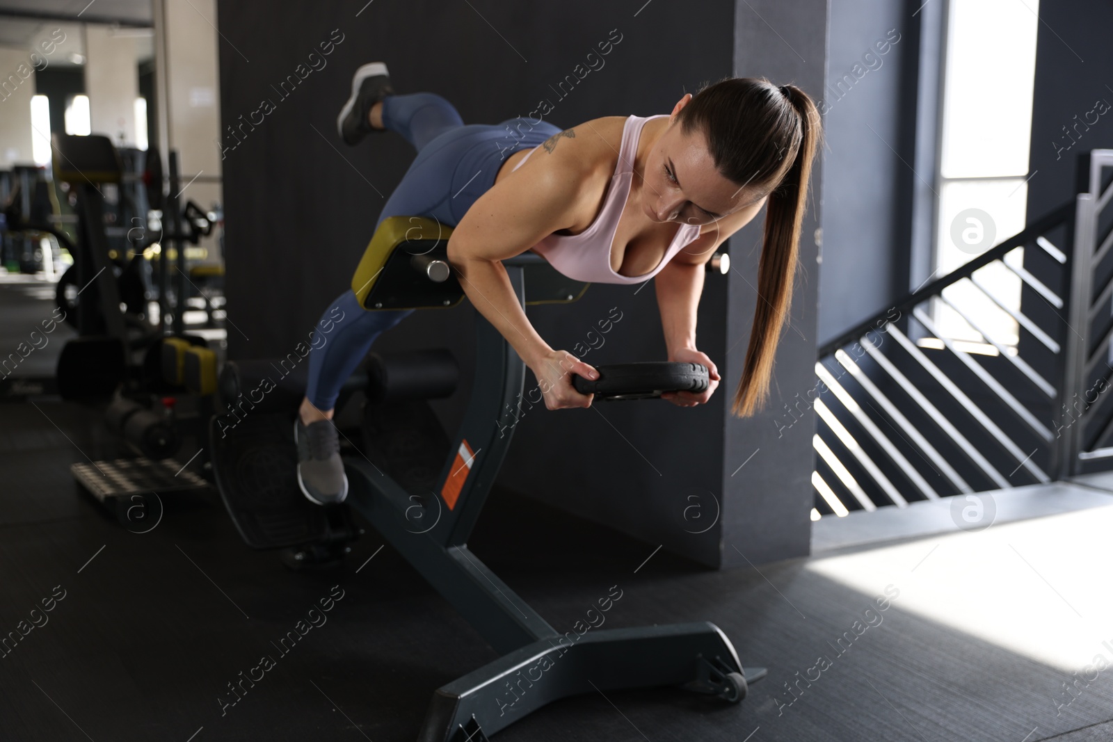 Photo of Athletic woman training with weight plate on t-bar row machine in gym