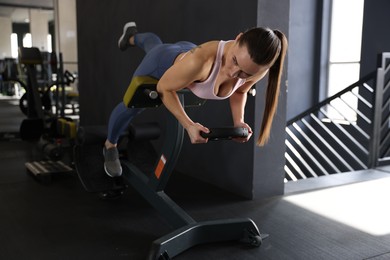 Athletic woman training with weight plate on t-bar row machine in gym