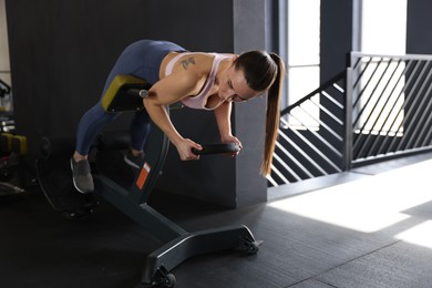 Photo of Athletic woman training with weight plate on t-bar row machine in gym