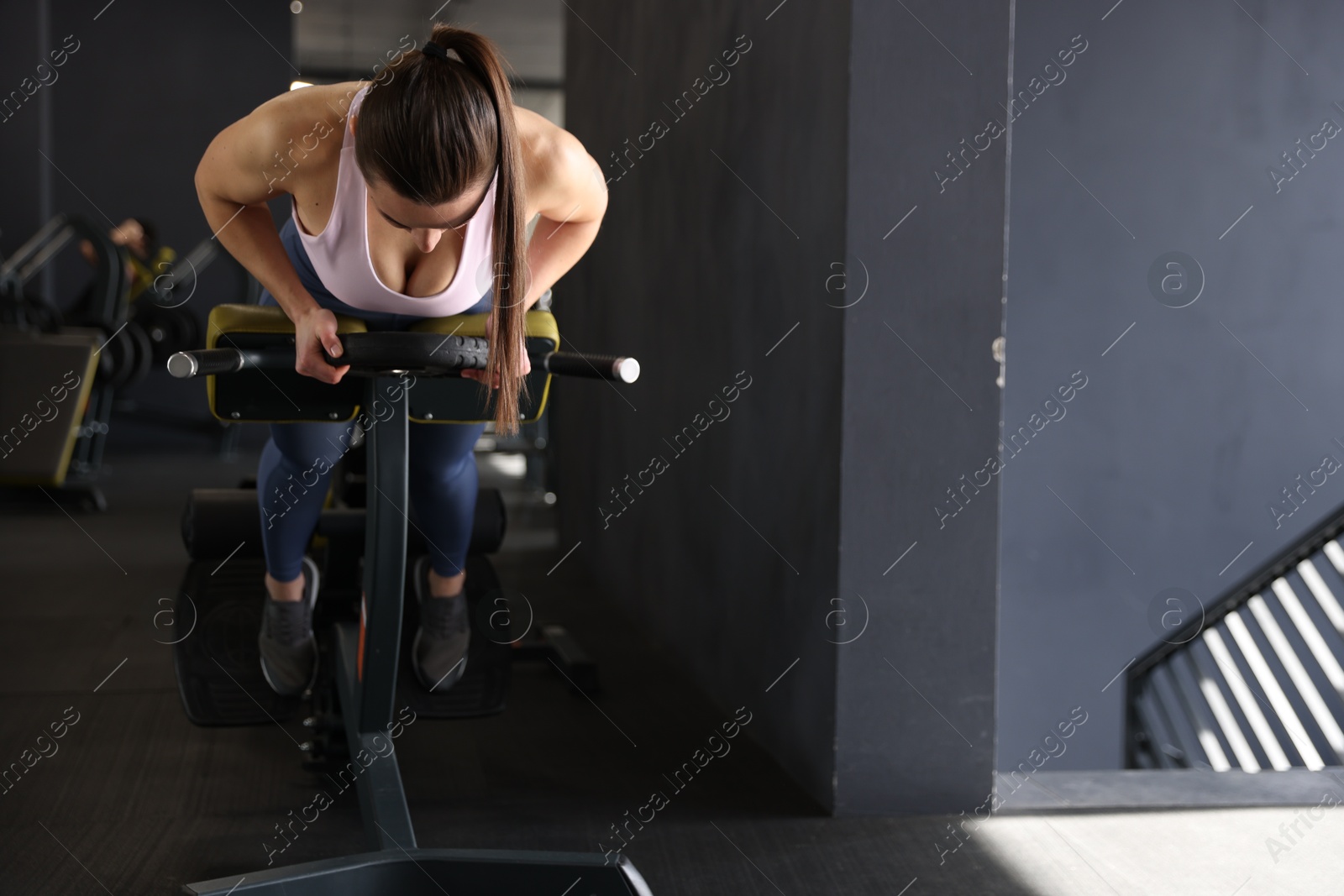 Photo of Athletic woman training with weight plate on t-bar row machine in gym. Space for text