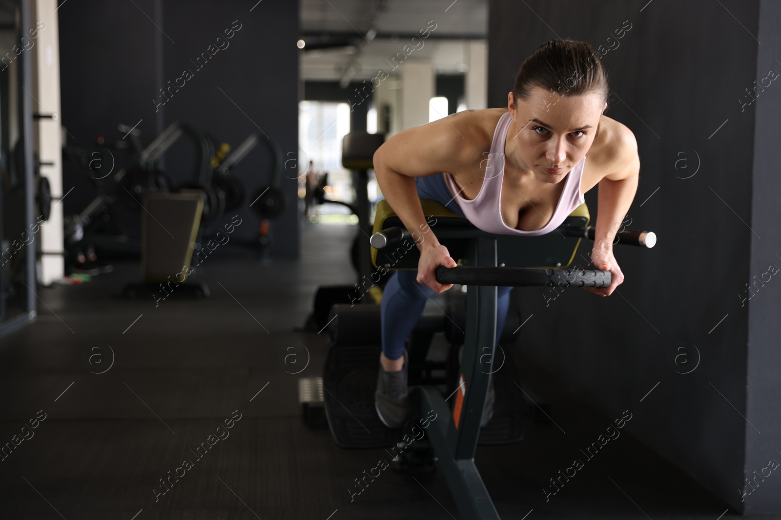 Photo of Athletic woman training with weight plate on t-bar row machine in gym. Space for text