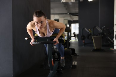 Athletic woman training with weight plate on t-bar row machine in gym. Space for text