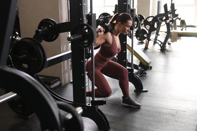 Athletic woman training with barbell on Smith machine in gym