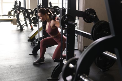 Photo of Athletic woman training with barbell on Smith machine in gym