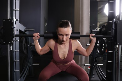 Photo of Athletic woman training with barbell on Smith machine in gym