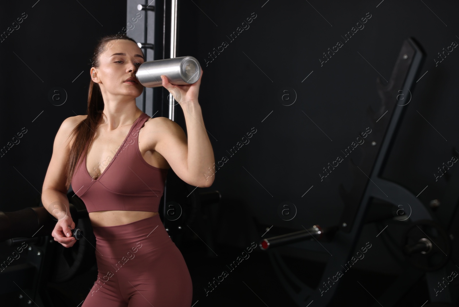 Photo of Athletic woman drinking from thermo bottle in gym. Space for text