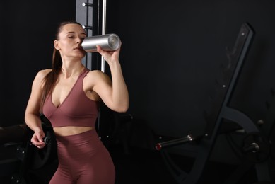 Athletic woman drinking from thermo bottle in gym. Space for text