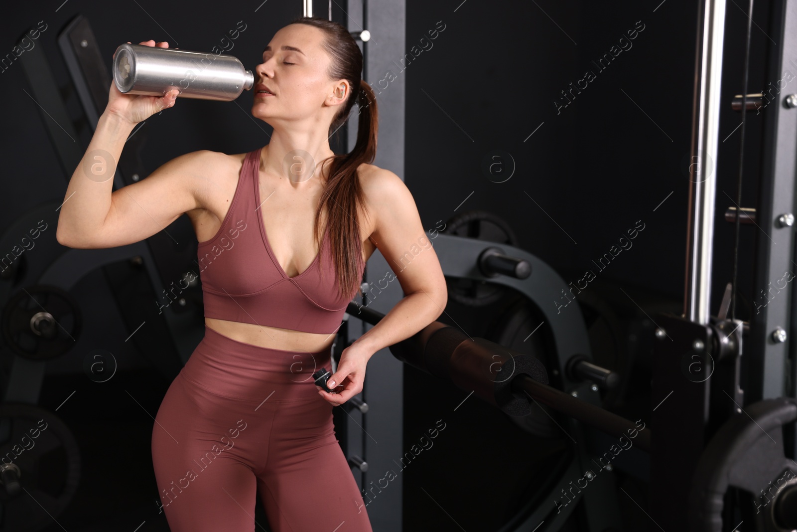 Photo of Athletic woman drinking from thermo bottle in gym. Space for text