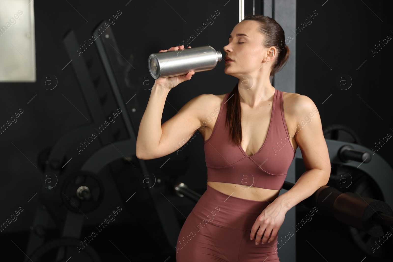 Photo of Athletic woman drinking from thermo bottle in gym. Space for text