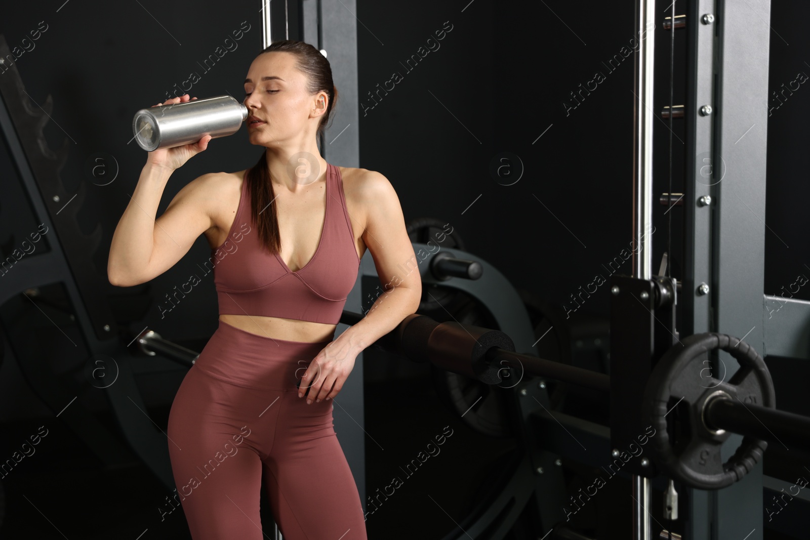 Photo of Athletic woman drinking from thermo bottle in gym. Space for text