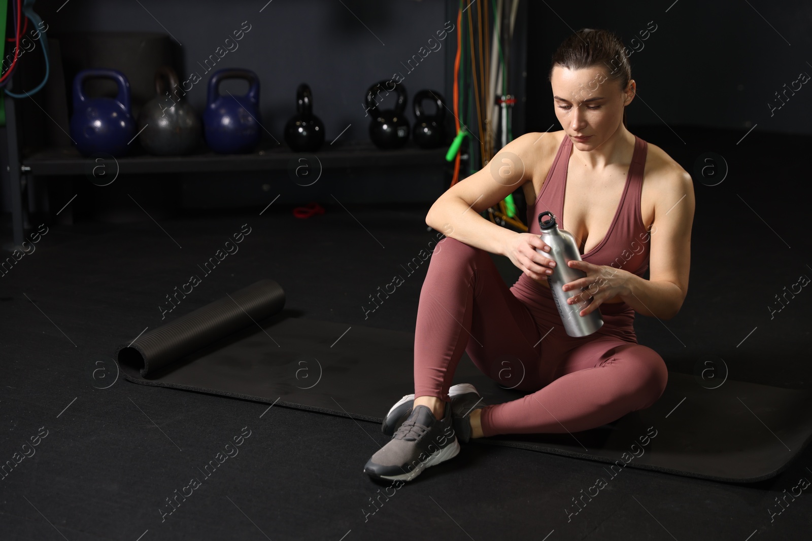 Photo of Athletic woman with thermo bottle sitting on yoga mat in gym. Space for text