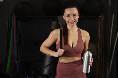 Smiling woman with thermo bottle in gym. Space for text