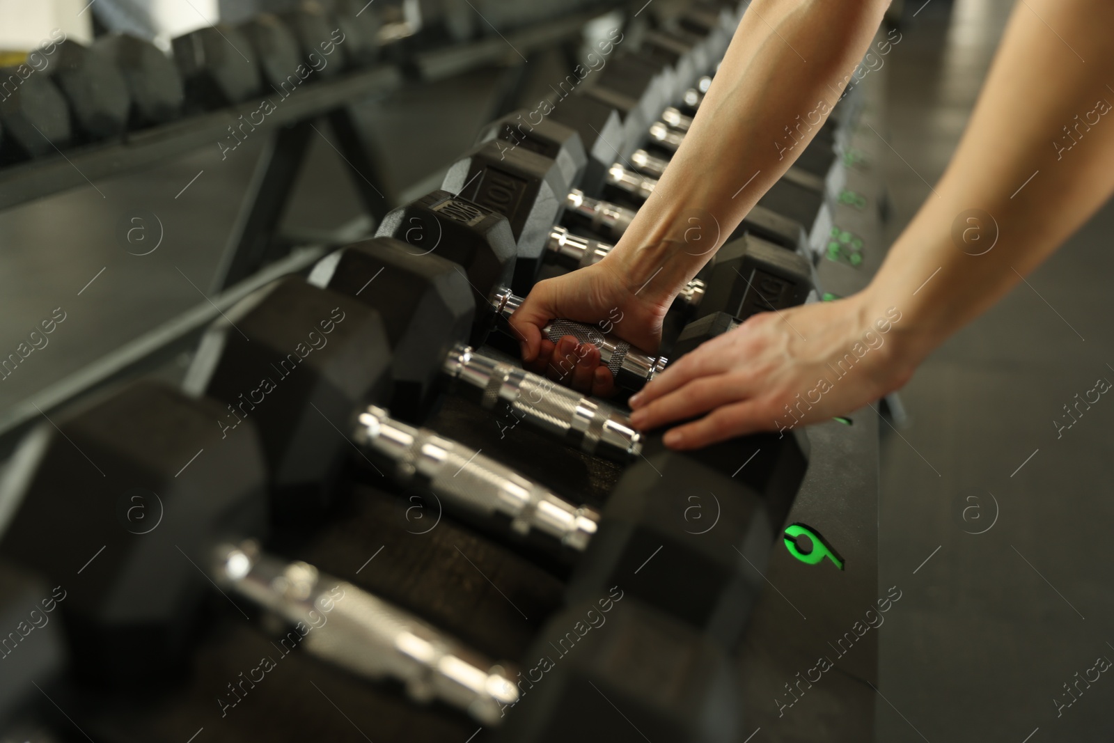 Photo of Woman taking rubber hex dumbbell in gym, closeup