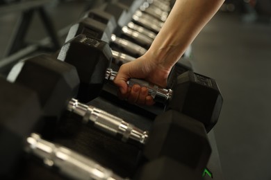 Woman taking rubber hex dumbbell in gym, closeup